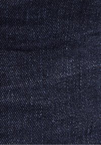 Gros plan sur un tissu en denim bleu foncé montrant une texture en armure diagonale et de subtiles variations de couleur.