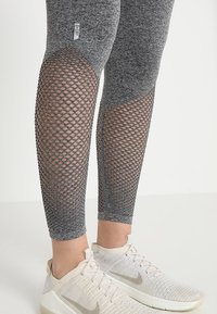 Szare legginsy z siateczkowymi wycięciami na łydkach, prezentujące teksturowany materiał. W zestawieniu z jasnymi trampkami z delikatnym logo.