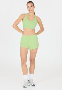 Ljusgrön idrotts-bra och shorts-set. Shortsen har resårmidja med dragsko. Slät textur, minimalistisk design.