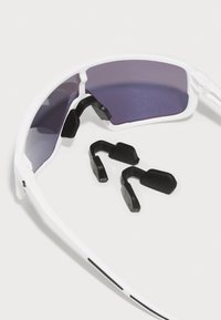 Weiße Sportsonnenbrille mit dunklen Gläsern, ausgestattet mit schwarzen Gumminasenpolstern und -bügelspitzen. Enthält zusätzliche schwarze Nasenpolster.