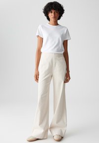 Weißes Baumwoll-T-Shirt, kombiniert mit hellbeigen Corduroy-Hosen mit weit geschnittenem Bein, die eine glatte Textur und ein hoch tailliertes Design aufweisen.