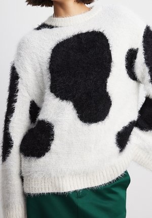 Witte fuzzy trui met grote onregelmatige zwarte vlekken gedragen met donkergroene broek.