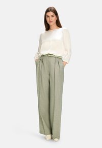 White silk blouse with puffed sleeves, paired with light green textured high-waisted trousers and a matching belt. Cream-colored shoes.