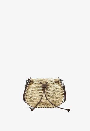 Bolso bandolera de paja beige tejido con cierre de cordón de cuero marrón oscuro y correa para el hombro sobre un fondo blanco.