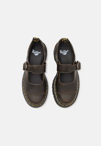 Paire de chaussures Mary Jane en cuir noir avec des brides à boucle et des coutures jaunes sur des semelles épaisses, vue de dessus.