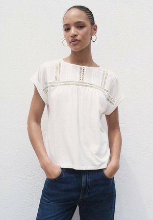 Witte blouse met korte mouwen, voorzien van textuur details en een relaxte pasvorm, gecombineerd met donkerblauwe jeans voor een casual look.