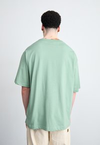 Minť zelena oversized tričko s krátkymi rukávmi a okrúhlym výstrihom, vyrobené z mäkkej tkaniny, pohľad zozadu ukazuje detail šitia.