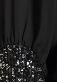 Abito nero con maniche a palloncino, caratterizzato da un polsino arricciato e texturizzato e una fascia di paillettes nere e argento scintillanti sul lato.