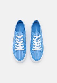 Sneakers in tela blu con strisce verticali bianche, lacci bianchi e suola in gomma. L'interno è anch'esso blu, offrendo un design coerente.
