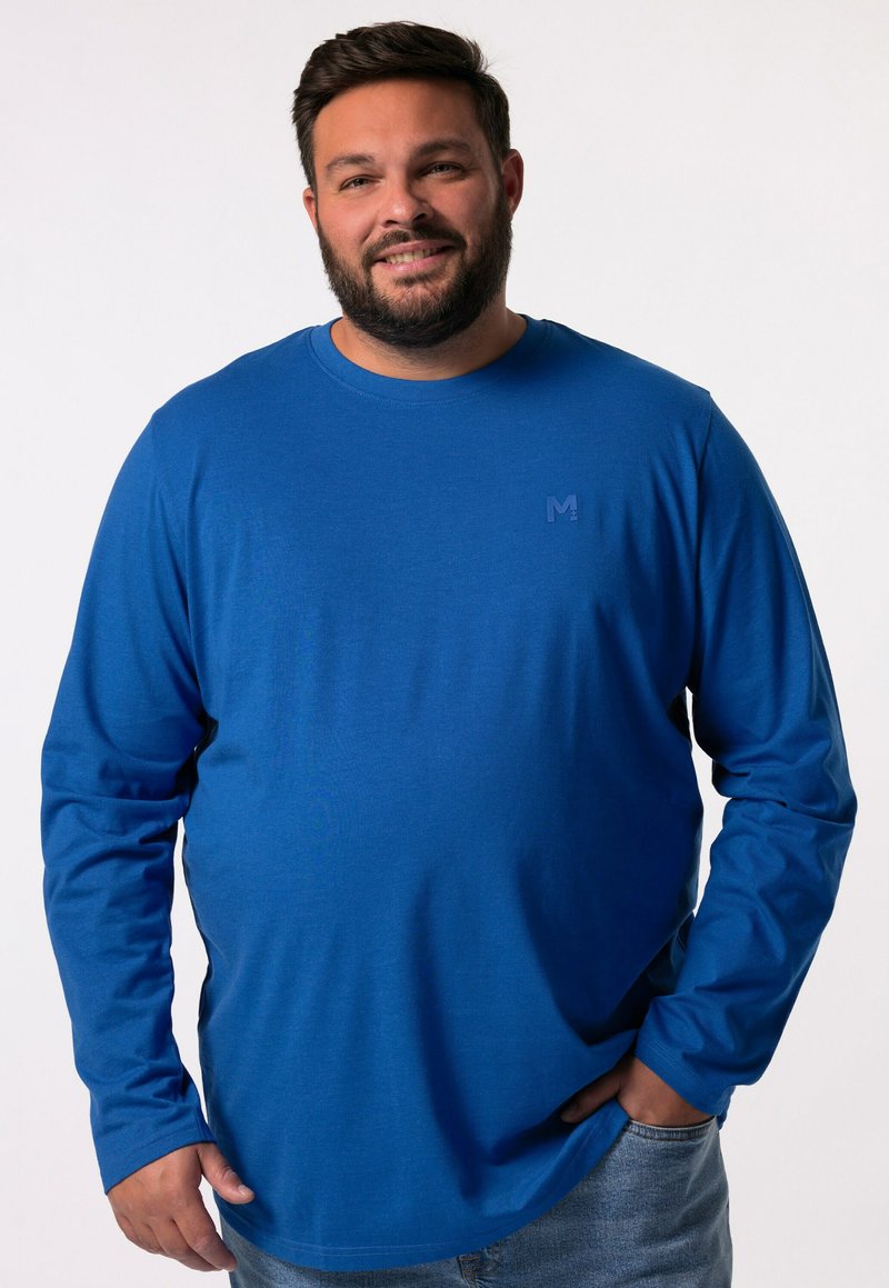 Camisa de manga larga y cuello redondo en tela azul sólida, con un pequeño logo en el pecho. El ajuste es holgado con detalles de costura visibles.