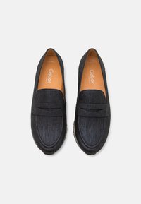 Svarta loafers med en texturerad läderovandel, ett dekorativt band över framsidan och en mjuk beige innersula. Flexibel sula för komfort.