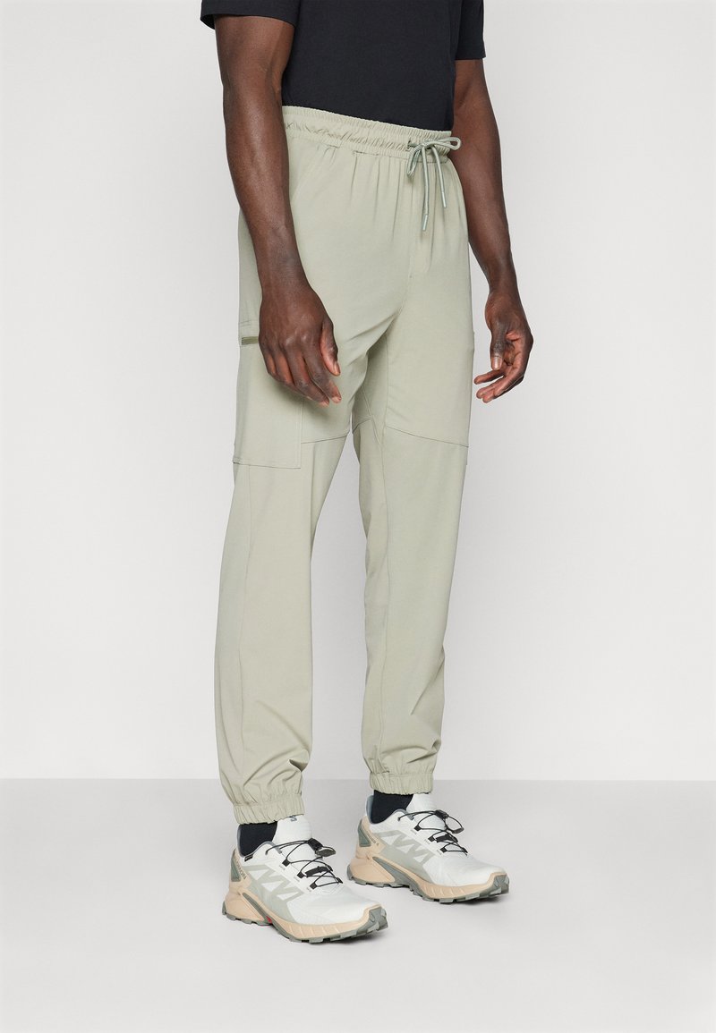 Pantalones verde oliva claros con cintura elástica y cordón, que cuentan con bolsillos laterales y puños ajustados, fabricados en tejido ligero.