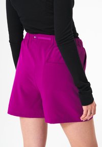 Fuchsiaschorts mit elastischem Bund und einer Gesäßtasche, aus glattem Stoff. Sichtbare Nähte entlang dem Saum.