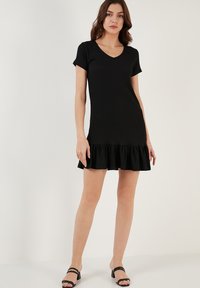 Black ribbed dress with a V-neck, short sleeves, and flared ruffle hem. Features a fitted silhouette, made from soft, textured fabric.