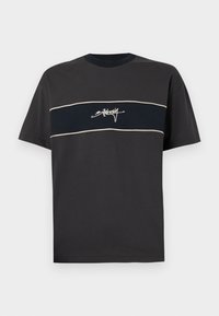Black cotton t-shirt with short sleeves, featuring a horizontal navy blue stripe and white outline with stylized text centered on the stripe.