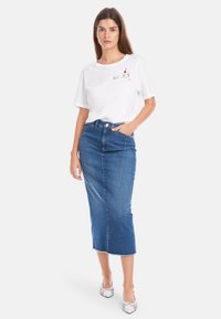 Weißes T-Shirt mit Grafikdesign, kombiniert mit einem blauen Jeansrock in mittellanger Länge mit geradem Schnitt und ausgefranstem Saum. Gestreifte Absätze.