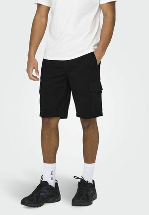 Schwarze Cargo-Shorts aus Baumwolle, mit Seitentaschen und lockerer Passform. Kombiniert mit einem weißen T-Shirt und schwarzen Sneakers.