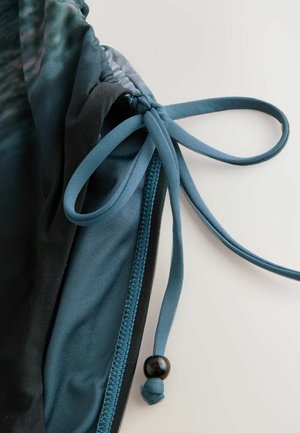 Fekete és türkiz fürdőruha húzózsinórral és állítható kötővel, sima textúrával és kontrasztos varrási részletekkel.