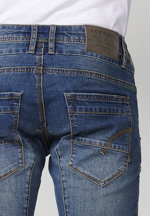 Blaue Denim-Jeans mit einer mittelhohen Taille, fünf Taschen, sichtbaren Nähten und einem Lederpatch auf der Rückseite mit Markennamen-Details.