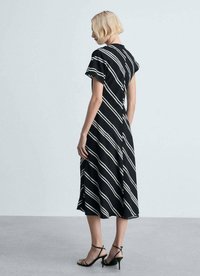 Robe noire avec des rayures blanches diagonales, manches courtes, ourlet au genou, tissu doux et coupe décontractée ; portée avec des talons noirs à lanières.