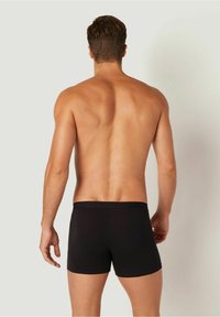 Svarta boxershorts i mjukt tyg med en mjuk midja och en figurnära design, sedda bakifrån mot en neutral bakgrund.