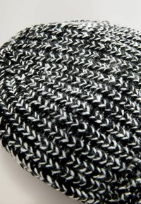 Pletene kape v črni in beli barvi, ki ima teksturiran vzorec z izmeničnimi debelimi in tankimi nitmi. Okrogla oblika z mehkimi robovi.