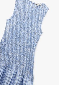 Sininen rypytetty mekko, jossa on tekstuuri, sisältää vartalonmyötäisen yläosan ja liehuvan ruudullisen hameen. Olkaimettoman muotoilun lisäksi takana on aukko.