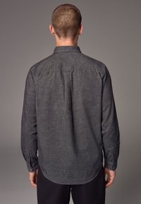 Camicia button-up grigia scura con tessuto testurizzato, maniche lunghe e orlo arrotondato. La camicia presenta un yoke posteriore e dettagli di cucitura sottili.