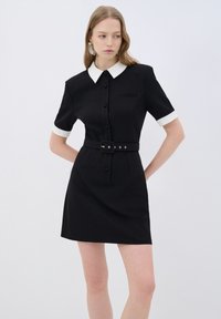 Schwarzes Kleid mit kurzen Ärmeln und weißem Kragen, mit tailliertem Schnitt, schwarzem Gürtel und Knopfverschluss, aus strukturiertem Stoff gefertigt.