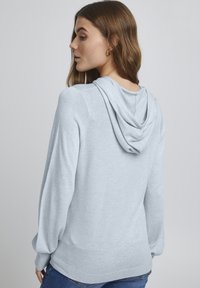 Jasnoniebieska bluza z kapturem o miękkiej teksturze, z luźnym krojem, długimi rękawami i wiszącym kapturem z tyłu. Prosty design, bez wzorów.