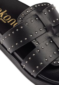 Sandal in pelle nera con cinturini incrociati adornati da borchie in argento. Suola spessa con leggera texture e bordi rialzati. Logo del marchio visibile all'interno.