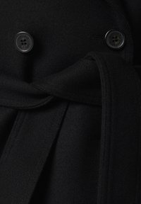 Czarny wełniany płaszcz z podwójnymi guzikami, paskiem w talii i gładką fakturą. Szczegóły stębnowania widoczne wzdłuż brzegów.