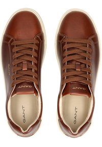 Zapatillas de cuero marrón con cordones marrones, punta redondeada y suela de goma blanca. Logo de GANT grabado en la lengüeta y en el lateral. Textura suave.
