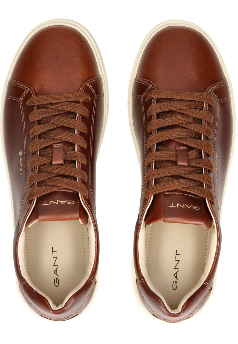 Sneaker in pelle marrone con lacci marroni, punta arrotondata e suola in gomma bianca. Logo GANT impresso sulla linguetta e sul lato. Texture liscia.