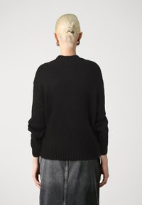 Maglione nero a maglia con una vestibilità rilassata, polsini e orlo a coste, indossato con una gonna in denim grigia. Tessuto testurizzato con un design casual e sovradimensionato.