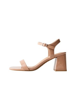 Beige sandal med åben tå, ankelrem, sølvspænde og blokhæl på hvid baggrund.