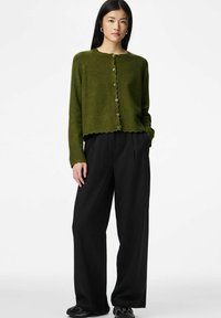 Zaļš adīts kardigans ar apaļu kakla izgriezumu, viļņotu apakšu un pogām priekšpusē; kopā ar melnā krāsā ar pinstrīpām platajiem biksēm.