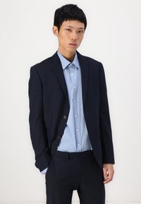 Sacou bleumarin cu dungi fine, cu două butoane, asortat cu o cămașă albastră deschis cu guler. Are rever notat și detaliu la buzunarul din față.