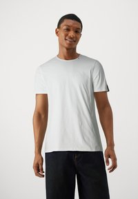 Hvid bomulds T-shirt med korte ærmer, rund halsudskæring og en sort detalje på ærmet, båret med mørkeblå jeans.