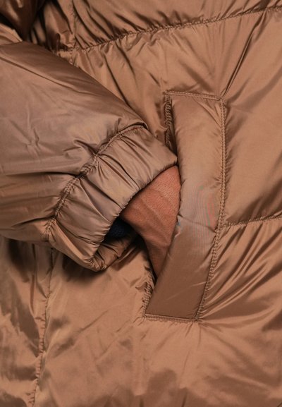 Casaco acolchoado castanho com uma textura lisa e brilhante. Apresenta punhos elásticos e um bolso lateral, evidenciando um design quente e isolado.