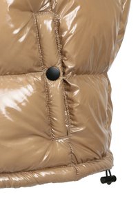 Puffermantel aus glänzendem tanfarbenem Material, mit einem schwarzen Druckknopf, gestepptem Muster und elastischem Saum mit Zugbändern zur Anpassung.