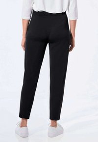 Schwarze Hosen mit geradem Schnitt und elastischem Bund, mit glatter Textur und figurbetontem Knöchellängen, kombiniert mit weißen Sneakern.