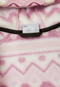 Rosa-weißer Fleece-Bereich mit geometrischen Mustern und einem Innenetikett, auf dem steht "Ich war hier:" über einer schwarzen Schlaufe.