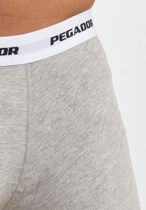 Close-up af en person iført lysegrå boxershorts med en hvid linning mærket "PEGADOR" med sort tekst.