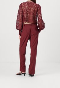 Top corto de encaje burdeos con mangas largas abullonadas, combinado con pantalones rectos a rayas diplomáticas a juego en burdeos y sandalias negras de tacón.