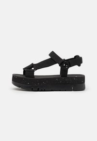 Sandalia de plataforma negra con correas de nylon ajustables, plantilla texturizada y suela de EVA moteada. Presenta un diseño moderno y minimalista.