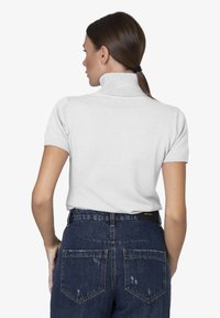 Maglione grigio chiaro a maniche corte con collo alto e finitura testurizzata, abbinato a jeans in denim scuro a vita alta con dettagli strappati.