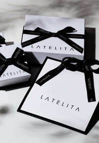 White gift boxes with black accents and ribbon, featuring the brand name "LATELITA" in a modern font. Various sizes stacked together.
