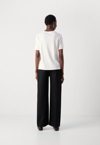 Witte top met korte mouwen en een rechte snit, gecombineerd met zwarte wijde broek met hoge taille, voorzien van een gestructureerd patroon en subtiele glans.