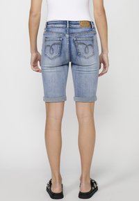 Shorts en denim bleu clair, coupe ajustée, ourlet roulé, deux poches arrière avec des coutures décoratives et une étiquette de marque en cuir à la taille.